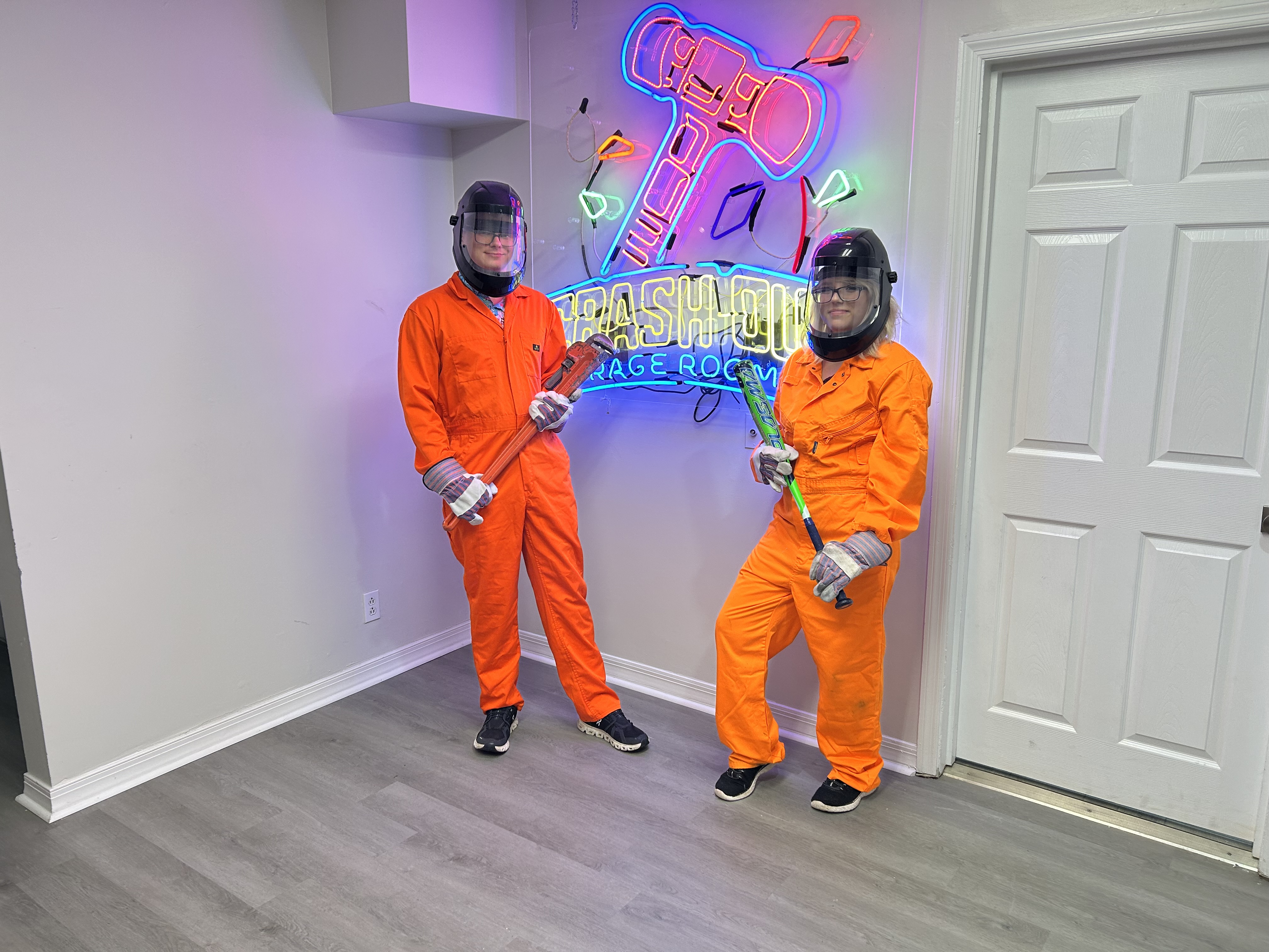Group of Crash Out customers in orange jumpsuits with bats in front of neon sign